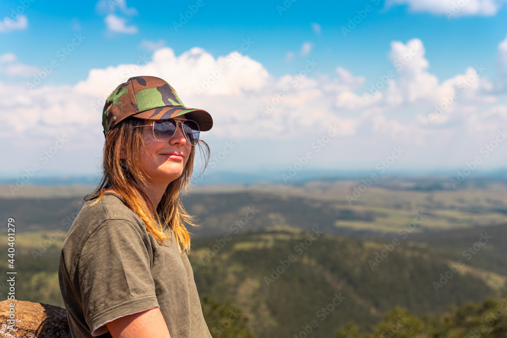 Naklejka premium Tourist girl hiker resting at the top of the mountain and enjoying amazing landscape view of mountains and beautiful sky