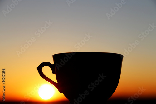Black silhouette of coffee cup on sunset background. Cozy atmosphere, view from the window to the sky with setting sun