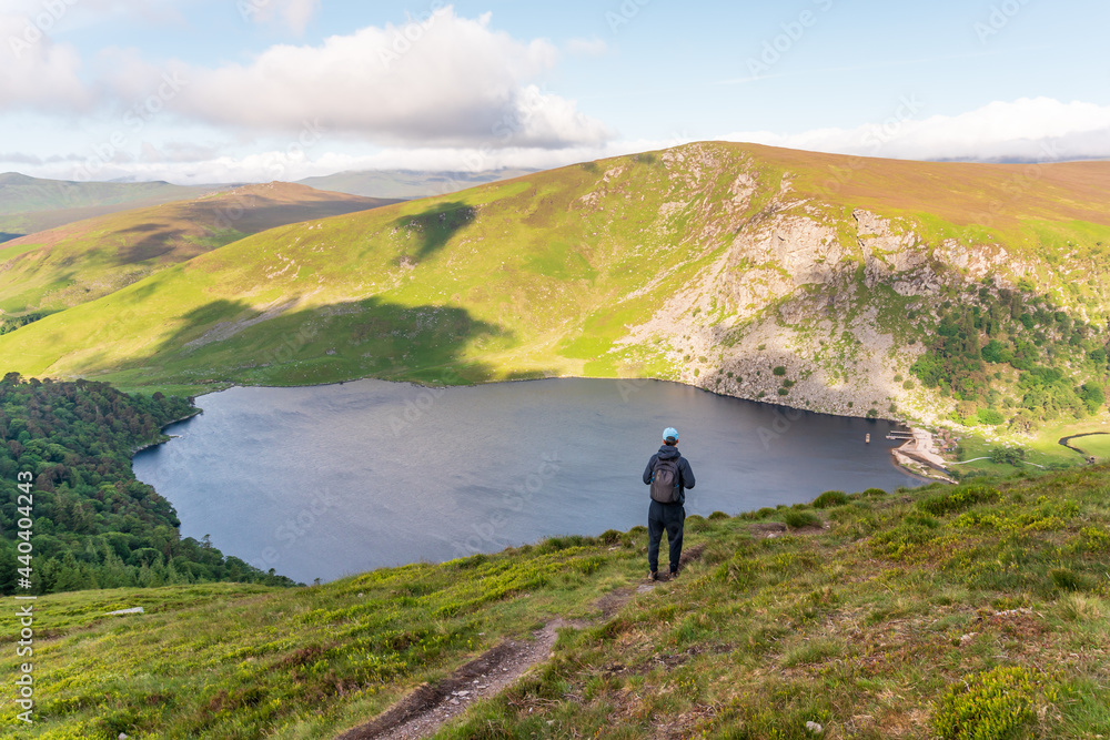 Hiker walking towards Lough Tay lake in Wicklow Mountains Ireland and enjoying the view on a summer morning.