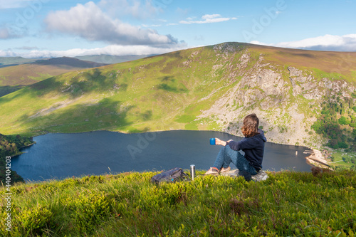 Woman having a cup of coffee and enjoying the view over Lough Tay after a hiking in Wicklow Mountains, Ireland
