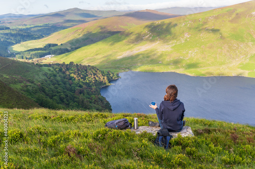 Woman having a cup of coffee and enjoying the view over Lough Tay after a hiking in Wicklow Mountains, Ireland