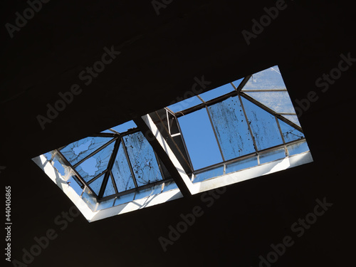 Old broken skylight in abandoned factory. Sunshine blue sky beyond dirty cracked glass. photo