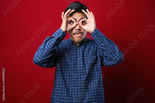 Young handsome man wearing casual shirt doing ok gesture like binoculars sticking tongue out, eyes looking through fingers. © Reza