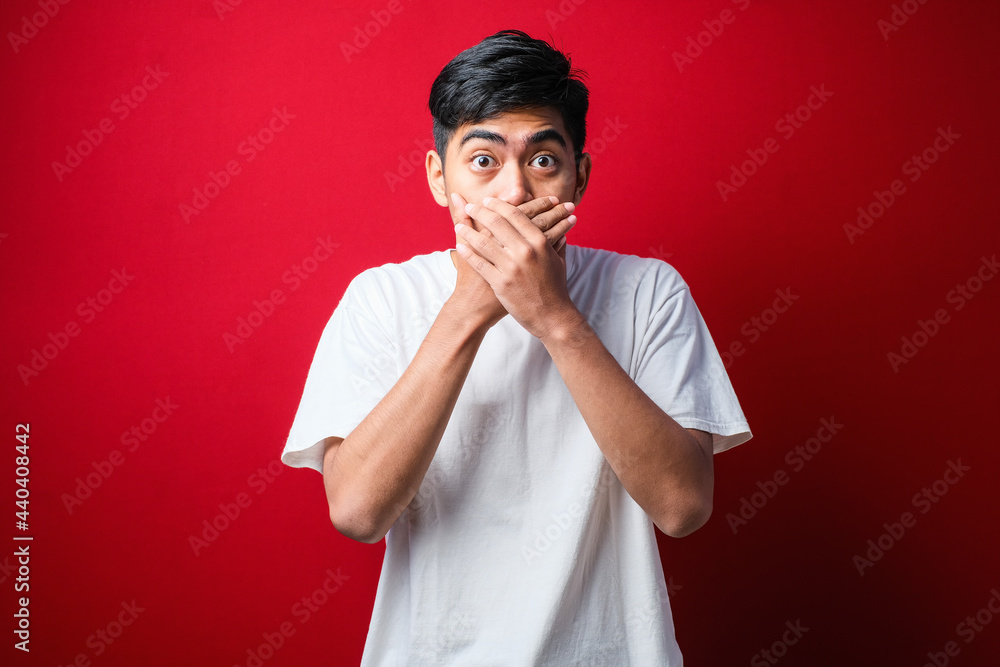 Young handsome man wearing white t-shirt over isolated red background shocked covering mouth with hands for mistake. Young handsome man wearing white t-shirt over isolated red background shocked covering mouth with hands for mistake.