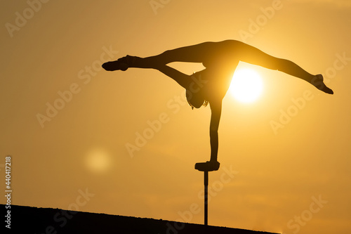 Silhouette of flexible acrobat doing handstand on the dramatic sunset background. Concept of willpower, control and dream