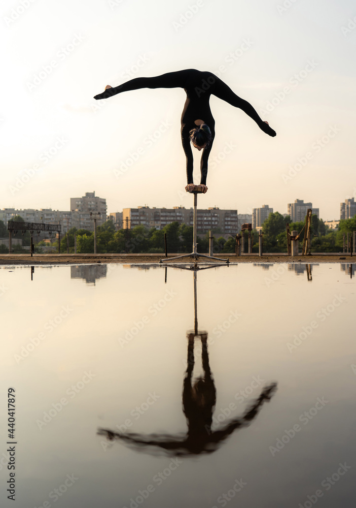 Silhouette of flexible acrobat doing handstand on the cityscape and sky background with reflection. Concept of individuality, creativity and outstanding