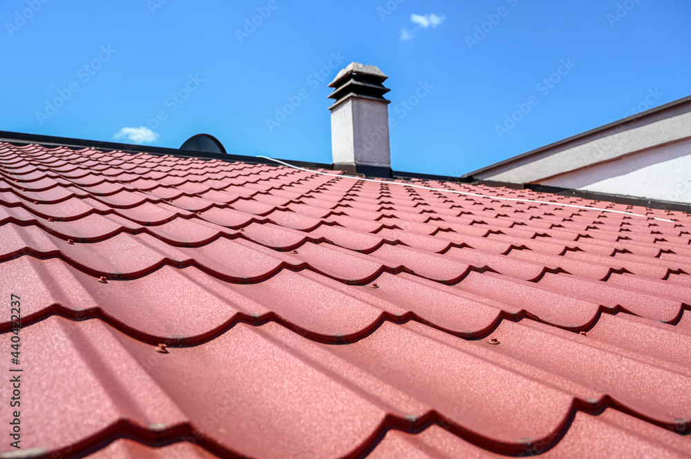 House roof. Red metal roof tiles. Roof made of metal sheets with cloudy sky in background. House roof. Red metal roof tiles. Roof made of metal sheets with cloudy sky in background.