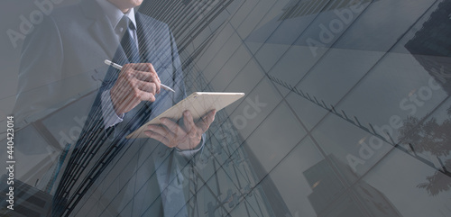 Double exposure of businessman using digital tablet computer with modern office buildings in the city, signing business contract, real estate development, business technology backgrounds