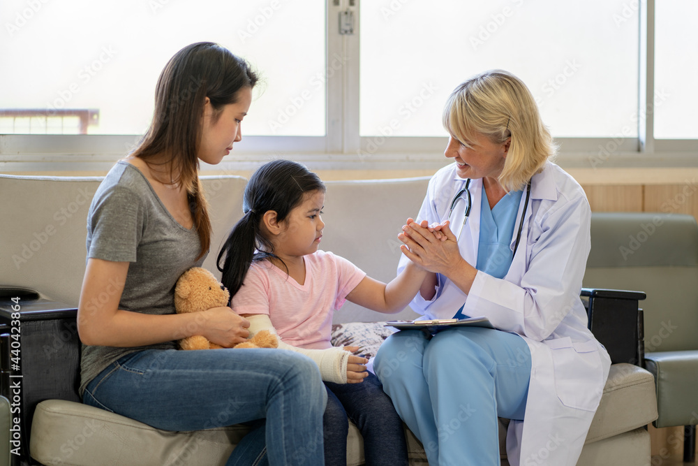 Pediatrician doctor examining little asian girl with a broken arm wearing a cast at hospital Pediatrician doctor examining little asian girl with a broken arm wearing a cast at hospital