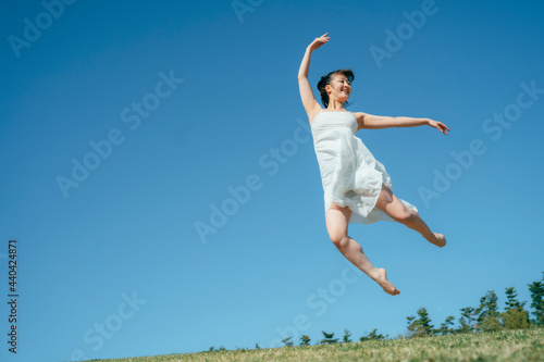 空と白いワンピースの踊る女性（ジャンプ）

