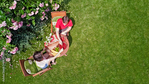 Young couple enjoying food and drinks in beautiful roses garden on romantic date, aerial top view from above of man and woman eating and drinking together outdoors in park

