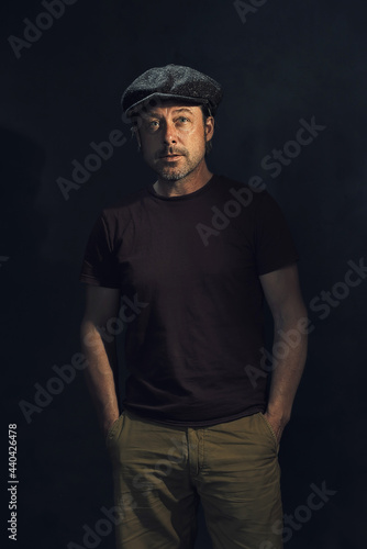 Dark portrait of a tough man with a cap and a gray stubble in a dark brown t-shirt. © ysbrandcosijn