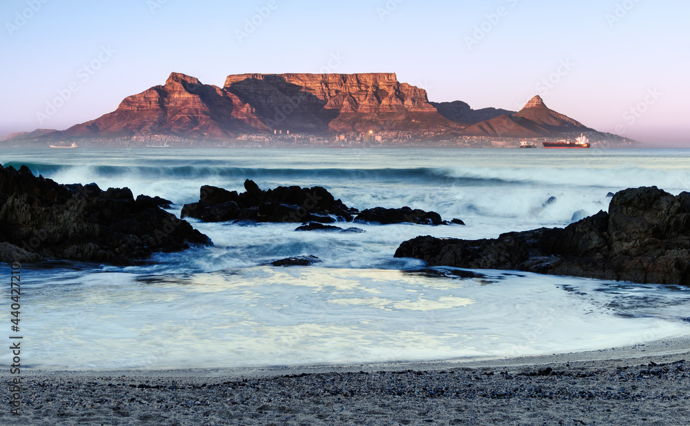 Fototapeta premium The mid winter sunrise lights up the front of Table Mountain as viewed from Bloubergstrand in Cape Town, South Africa.