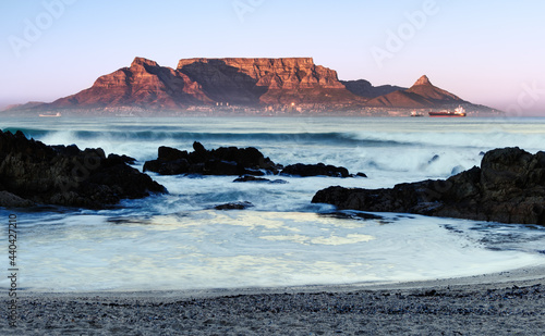 The mid winter sunrise lights up the front of Table Mountain as viewed from Bloubergstrand in Cape Town, South Africa.