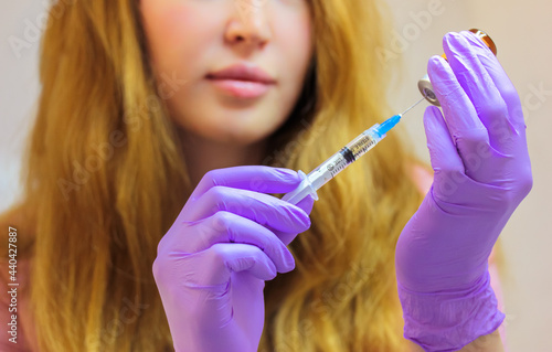 A young woman doctor wearing purple rubber gloves holds an injection syringe with a thin needle. Lip augmentation procedure, facial, body rejuvenation, mesotherapy. Aesthetic cosmetology. Beauty Salon