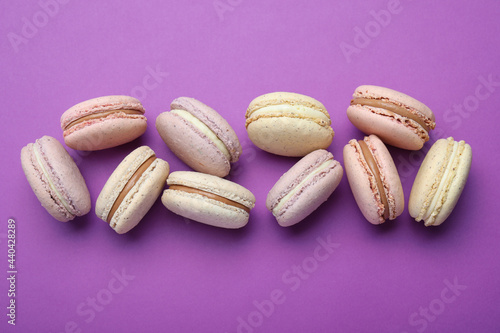 Delicious colorful macarons on purple background, flat lay