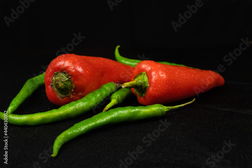 Red and green peppers on a black background. Black fabric background in folds.