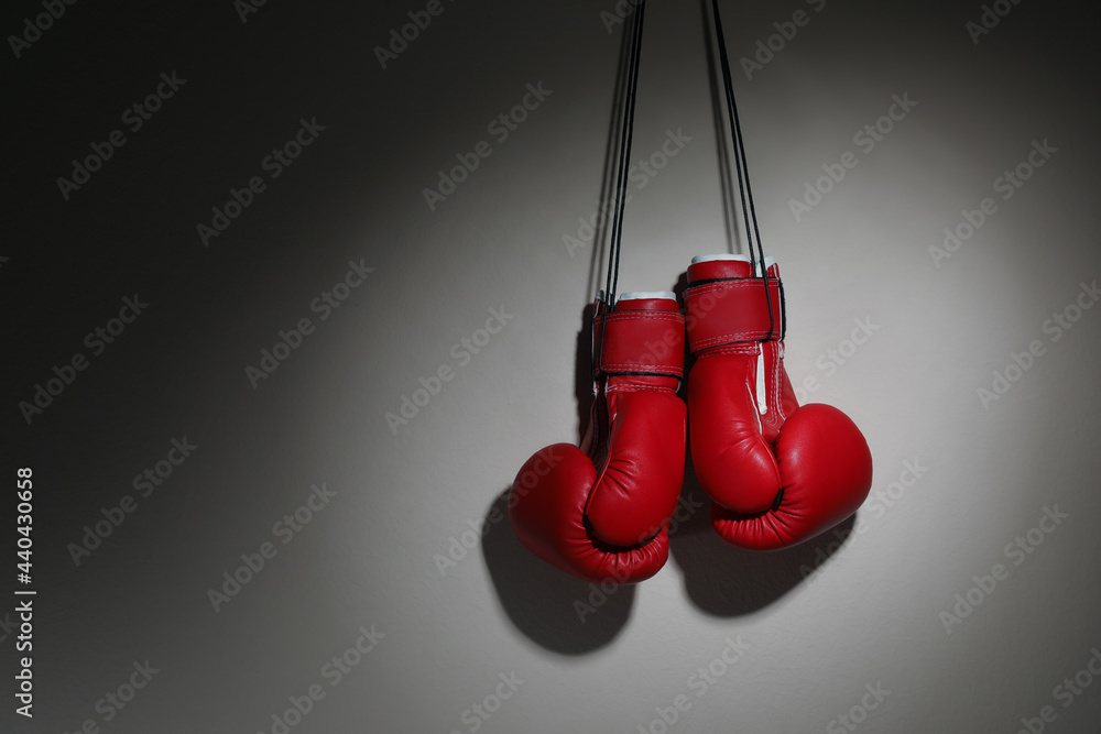 Pair of boxing gloves hanging on beige wall, space for text
