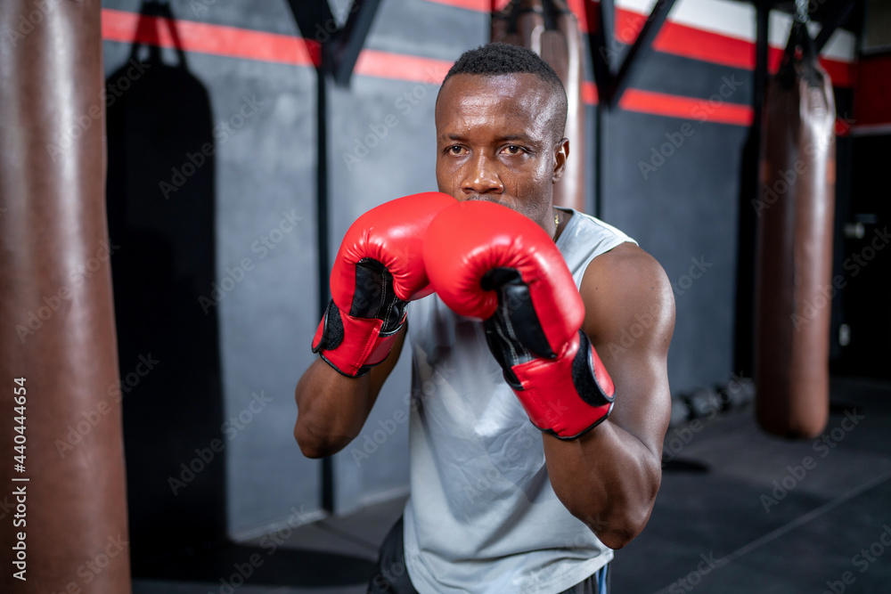 African American fighter man wear boxing red gloves and punching forward with one fist to camera in the fitness sport gym. Make looking forward with serious face. Exercise for a healthy body