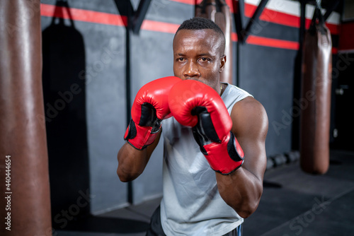 African American fighter man wear boxing red gloves and punching forward with one fist to camera in the fitness sport gym. Make looking forward with serious face. Exercise for a healthy body