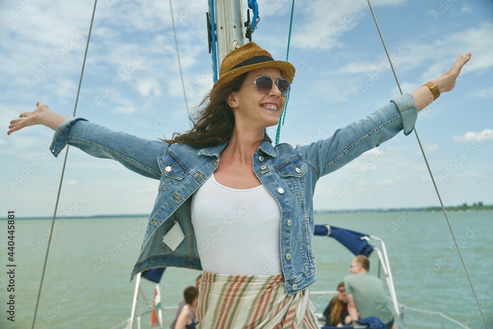 Happy young woman relaxing on sailing boat enjoying summer vacation. Wind, hat, sunglasses, traveling.