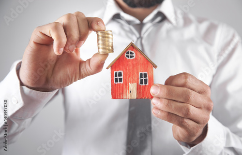 Businessman holding house model and coins.