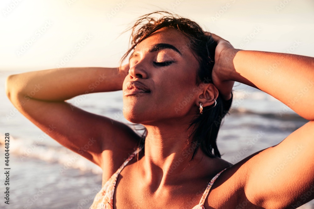 © Davide Angelini - Cheerful black woman enjoying sunset on the beach - African female with closed eyes relaxing outdoor