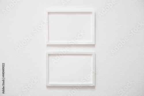 front view of two blank white horizontal photo frames hanging on clean white cement wall, interior design background concept.