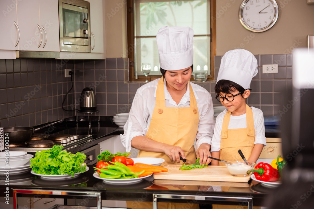 Asian woman young mother with son boy cooking salad food with vegetable holding tomatoes and carrots, bell peppers on plate for happy family cook food enjoyment lifestyle kitchen in home Asian woman young mother with son boy cooking salad food with vegetable holding tomatoes and carrots, bell peppers on plate for happy family cook food enjoyment lifestyle kitchen in home