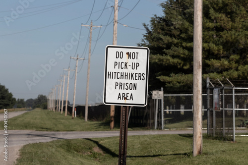 Фотография DO NOT PICK UP HITCHHIKERS PRISON AREA sign near a correctional facility along a deserted highway