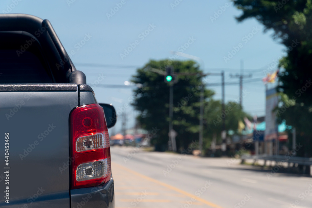 Back side of pick up car gray color on the asphalt road. Blurred vision of road traffic lights at the intersection. Green traffic lights cars can pass. during the day in Thailand.