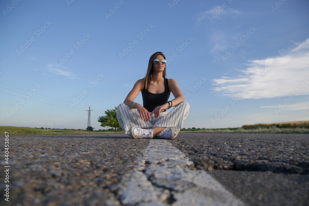Portrait of a beautiful teenage girl with cool attitude sitting on the road with blue sky behind