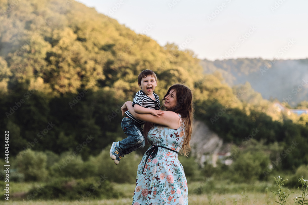 Mother and child in chamomile field on vacation. Beautiful family and joy of motherhood. Young mother hugs her son tightly and he laughs with pleasure and embarrassment.