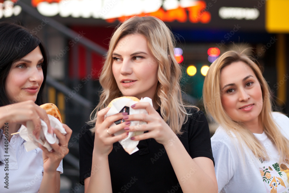 Pretty young women eating hamburger outdoor on the street