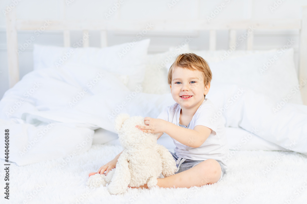 a child with a teddy bear on the bed at home plays and laughs a child with a teddy bear on the bed at home plays and laughs