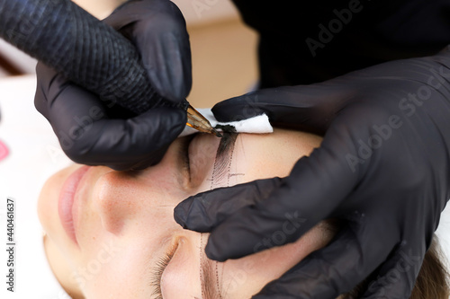 permanent makeup artist performs eyebrow tattooing by holding the eyebrow with his hand and stretching the skin © Roman