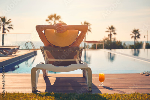 Canvas Print Rear view woman wear hat sunbathing on deckchair on poolside