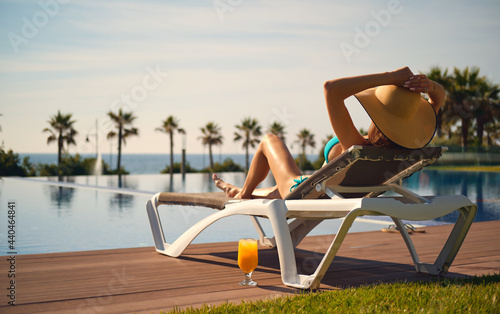 Canvas Print Rear view woman wear hat sunbathing on deckchair on poolside