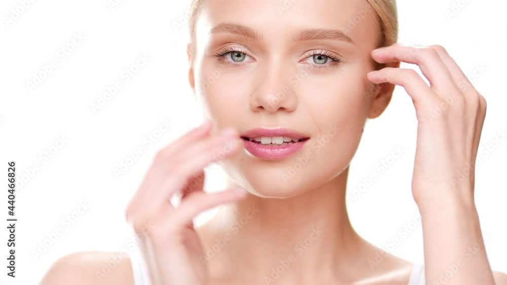 Close-up beauty portrait of beautiful blonde European girl in white top touches her jaw line and turns her head to the right smiling wide for the camera on white background | Skin moisturizing concept Close-up beauty portrait of beautiful blonde European girl in white top touches her jaw line and turns her head to the right smiling wide for the camera on white background | Skin moisturizing concept
