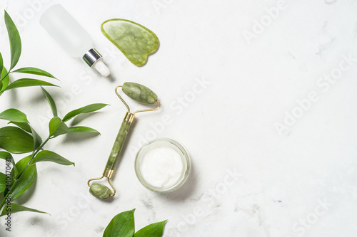 Scincare product. Jade roller and gua sha stone massager with face cream and serum bottle. Anti aging therapy. Top view.