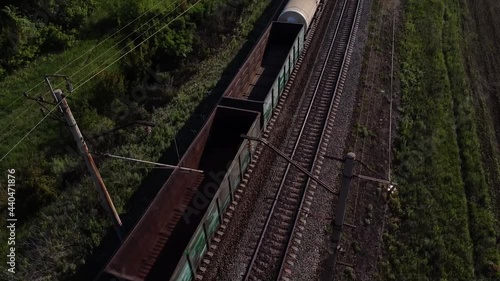 Railway transport. The locomotive pulls many different cars. Transportation of various goods. Green fields background. The video was taken from a drone.