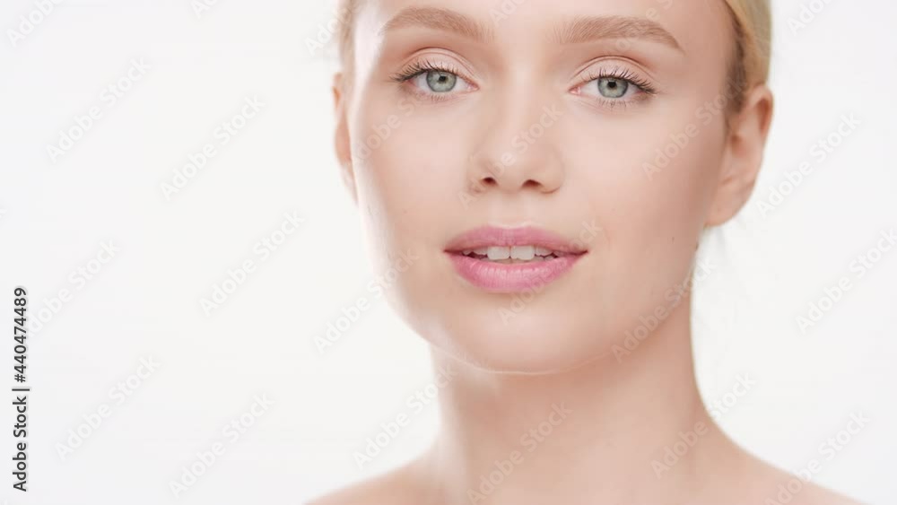 Big close-up shot of beautiful slim Caucasian young woman with long blonde hair in ponytail in white crop top touches her clavicle smiling wide for the camera on white background | Skincare ad Big close-up shot of beautiful slim Caucasian young woman with long blonde hair in ponytail in white crop top touches her clavicle smiling wide for the camera on white background | Skincare ad