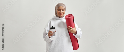 Fototapeta Naklejka Na Ścianę i Meble -  Happy young arabian woman in hijab holding sport mat