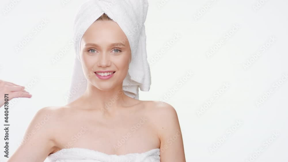 Beautiful Caucasian young fit woman wrapped in a towel touches her clavicles after taking a bath turning her body and smiling wide for the camera on white background | Body cream commercial Beautiful Caucasian young fit woman wrapped in a towel touches her clavicles after taking a bath turning her body and smiling wide for the camera on white background | Body cream commercial