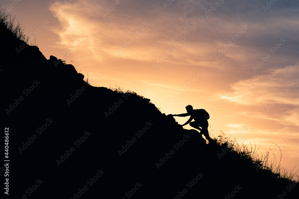 Silhouette of man climbing up mountain. 