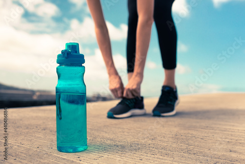 Drinking water exercise concept. Female runner tying her shoe next to bottle of water.	