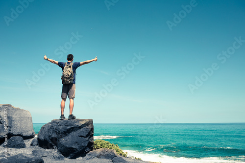 Male hiker on cliff edge looking out to the blue ocean. Freedom in nature concept. 