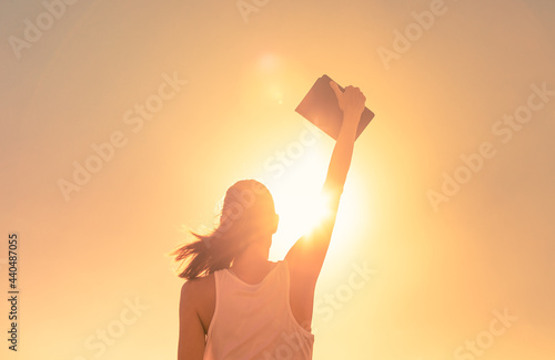 Fototapeta Young woman holding book, bible celebrating success, and feeling happy accomplishing her goals