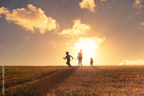 Mother and her children running playing in the park at sunset. 