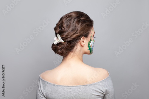 Nice woman back and head with perfect updo hairdo and painted flowers on her skin on gray background